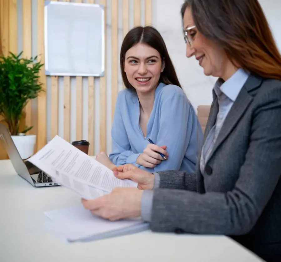 dwie kobiet śmiejące się jedna trzyma w ręku długopisy druga kartki papieru